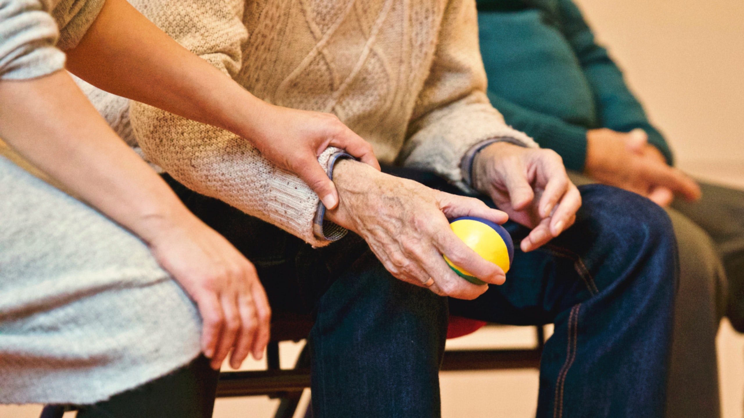 Aide helping person hold a ball during physical therapy